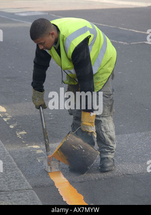 Jeune homme peinture à la main seule ligne jaune sur route avec électrique d'outil de marquage à chaud et peinture, Cheam, le sud de Londres, Angleterre Banque D'Images