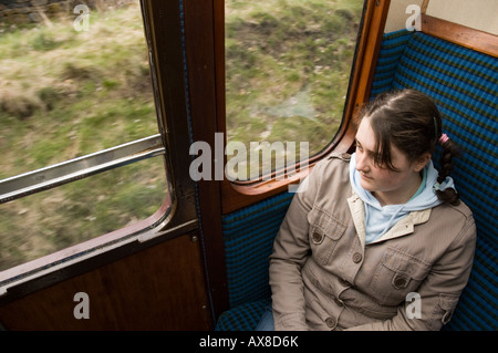 Teenage girl staring hors d'un train. Le train circule sur le chemin de fer de la vallée d'une valeur dans le West Yorkshire, Angleterre, Royaume-Uni. Banque D'Images