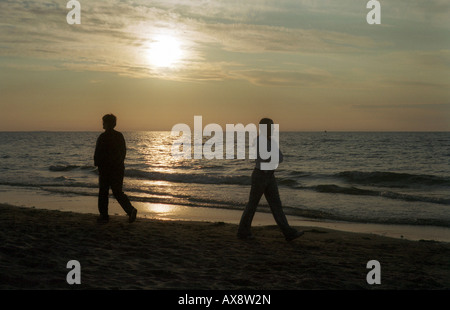 La femme et l'homme passe outre à une plage au coucher du soleil à Miedzyzdroje, Pologne Banque D'Images