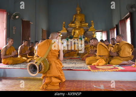 Un novice moine thaïlandais avec un bol d'aumône sur son dos, s'agenouille devant les moines du temple dans le cadre de son ordination Banque D'Images