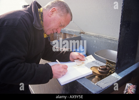 Pêcheur en bord de mer en remplissant les formulaires nécessaires à partir de la vente locale des poissons fraîchement pêchés sur front de mer par Goring Banque D'Images