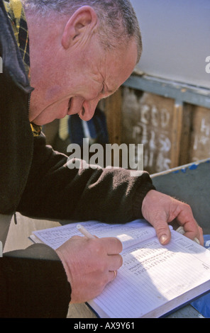 Pêcheur en bord de mer en remplissant les formulaires nécessaires à partir de la vente locale des poissons fraîchement pêchés sur front de mer par Goring Banque D'Images