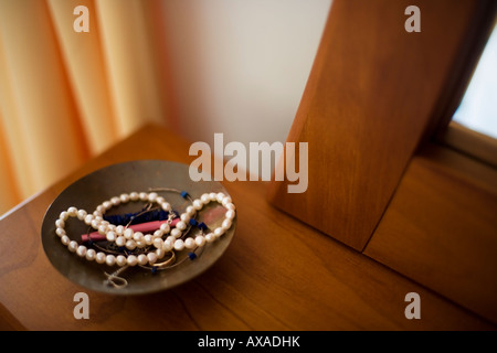 Collier de perles en laiton bol sur sol en bois commode avec boucles d'oreille et anneau de mariage Banque D'Images