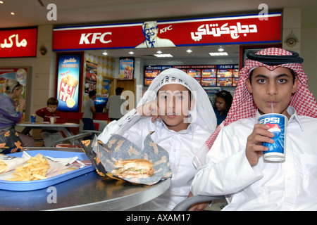 Enfants qatariens en tenues traditionnelles eating fast food dans un centre commercial de Doha. Banque D'Images