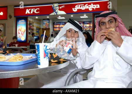 Enfants qatariens en tenues traditionnelles eating fast food dans un centre commercial de Doha. Banque D'Images