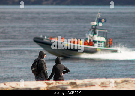 Jeune couple aimant holding hand tout en regardant les touristes à bord de 'Croisières AML' sur le bateau pneumatique de l'estuaire de la rivière Saguenay [] Banque D'Images