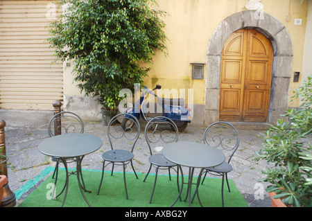 Quatre chaises à l'extérieur d'un restaurant avec une vespa scooter stationné sur le mur à l'arrière Banque D'Images