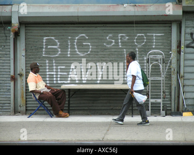 Homme assis en face de volets d'un atelier fermé à la 125 rue à Harlem, USA, Manhattan, Harlem, New York Banque D'Images