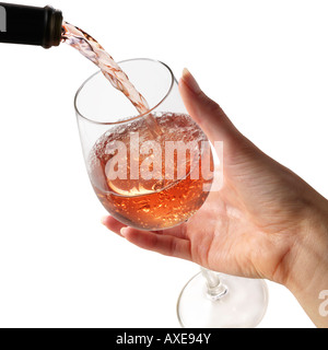 Vin rose est versé dans un verre de vin étant détenu par une main de femme sur un fond blanc. Banque D'Images