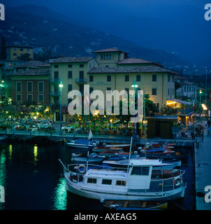 Waterfront port de Malcesine au crépuscule avec des restaurants les bateaux avec des collines en arrière-plan sur le Lac de Garda Lombardie Province Italie Banque D'Images