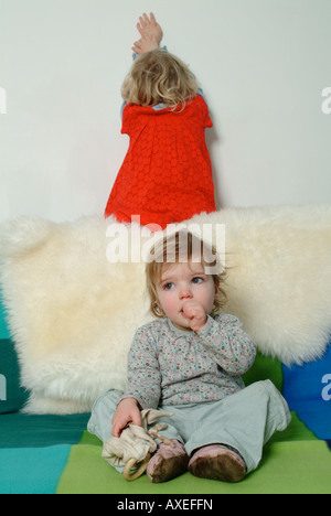 Deux petites filles assise sur le canapé, l'un de sucer son pouce, l'autre de bouder. Banque D'Images