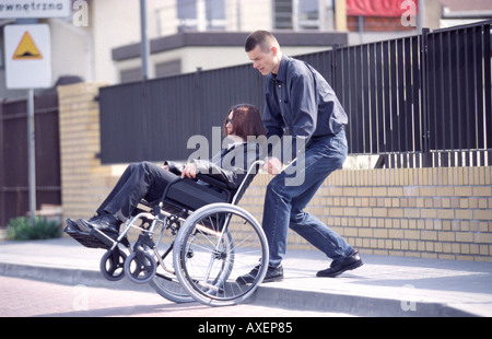 Jeune homme avec une femme handicapée sur un fauteuil roulant dans la rue. Banque D'Images