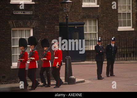 Quatre gardes Grenadiers le long de cour en mars Stable St James' Palace, Londres sous la surveillance de deux policiers métropolitains. Banque D'Images