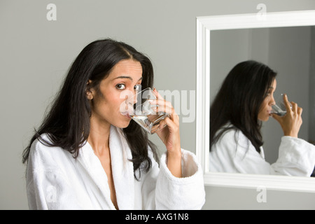 Une jolie jeune femme à boire de l'eau avant son reflet dans un miroir Banque D'Images