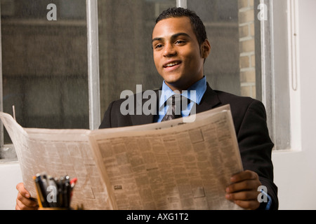 Smiling young business man sitting par une fenêtre avec un journal Banque D'Images