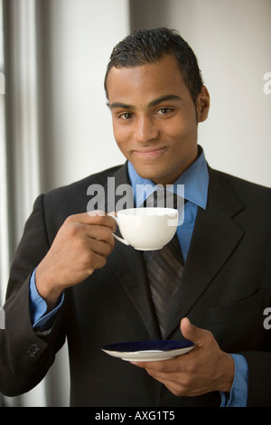 Smiling young man drinking tea tenant une tasse et soucoupe et vêtu d'un costume Banque D'Images