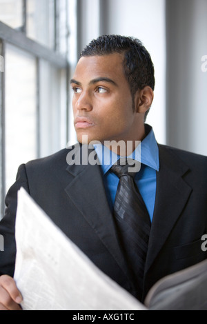 Un jeune homme d'affaires lire un journal par une fenêtre en costume et l'heure Banque D'Images