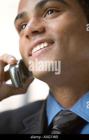 Séduisant jeune homme sourit tout en parlant au téléphone. Il porte un costume et une cravate. Banque D'Images
