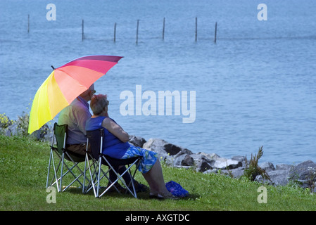 Couple de personnes âgées assis sous un parasol et regardant la mer Banque D'Images