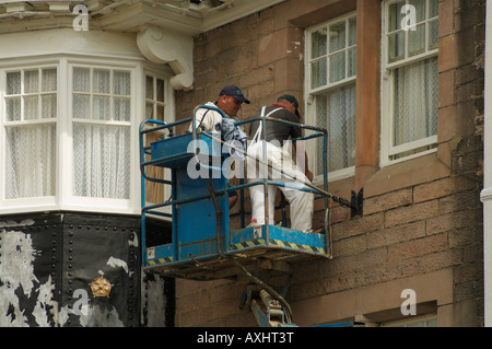 Deux ouvriers qui décorent l'extérieur d'un bâtiment de l'hôtel debout sur une nacelle Banque D'Images