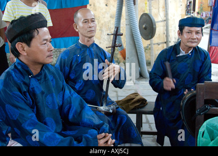 Trois musiciens vêtus de ao dai traditionnel jouant des instruments traditionnels vietnamiens pour les esprits des défunts Banque D'Images