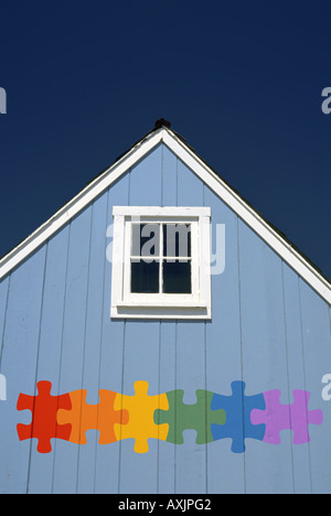 Peu de lumière blue house gable avec carré blanc peu de fenêtre et d'une scie sauteuse en pièces de puzzle couleurs arc-en-ciel Banque D'Images