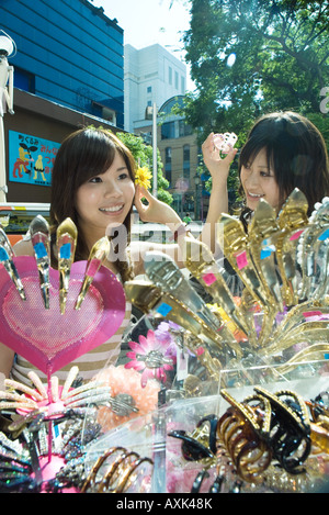 Deux jeunes femmes dans la rue du marché, en essayant sur Accessoires cheveux, smiling Banque D'Images