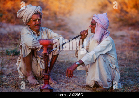 Deux hommes Indiens bénéficiant d'un tuyau de fumer de l'opium, à la fin de la journée au crépuscule dans la campagne près de Delhi Inde Banque D'Images