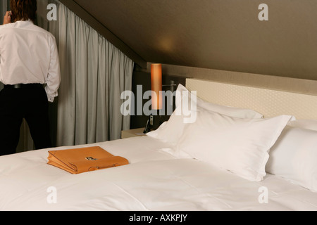 Businessman standing dans une chambre d'hôtel, à l'aide d'un téléphone portable, vue arrière Banque D'Images