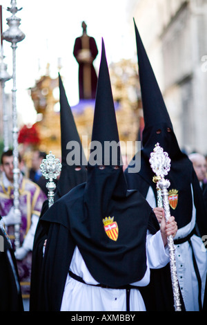 Pénitents cagoulés portant bâtons avec leur emblème de la fraternité en face d'un flotteur à l'image de Christ. Banque D'Images