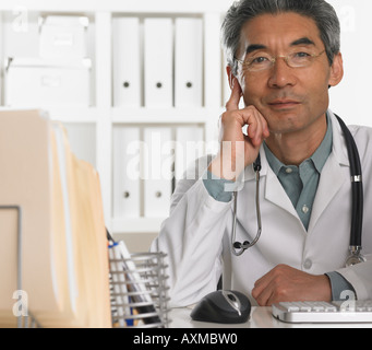 Senior male doctor sitting at desk Banque D'Images