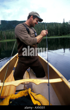 Un pêcheur de mouche dans les pataugeoires imperméables pantalons est à genoux dans un canot d'amorce son crochet dans le lac distant dans Eva Inside Passage au sud-est de l'Alaska USA Banque D'Images