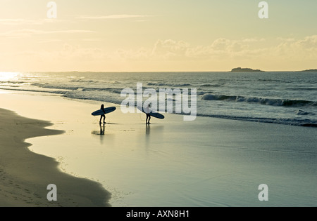 Surfeurs transportant des planches de surf marchant le long de la plage de sable fin le soir de l'été léger. White Rocks Strand, Portrush, Irlande Banque D'Images