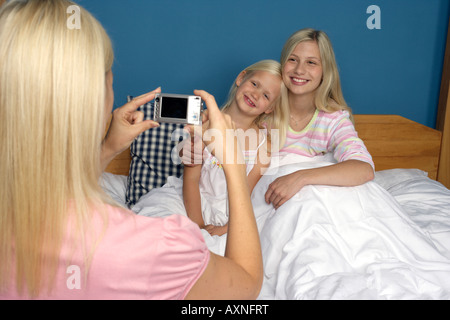 Femme blonde de prendre une photo de ses deux filles qui sont assis au lit, close-up Banque D'Images