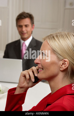 Young blonde woman is phoning en face d'un homme qui travaille avec un ordinateur portable, selective focus Banque D'Images