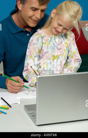 Homme assis derrière un ordinateur portable avec sa fille pendant le dessin dans un carnet Banque D'Images