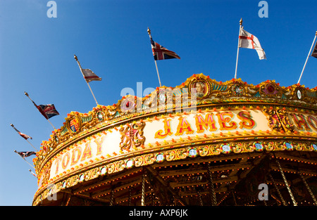 Fairground carousel avec merry-go-round en rayures coloré et l'or avec des drapeaux sous ciel bleu aujourd'hui vieux signe james Banque D'Images