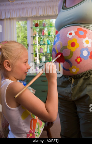 Jeune fille peint des fleurs sur le ventre de femme enceinte USA Banque D'Images