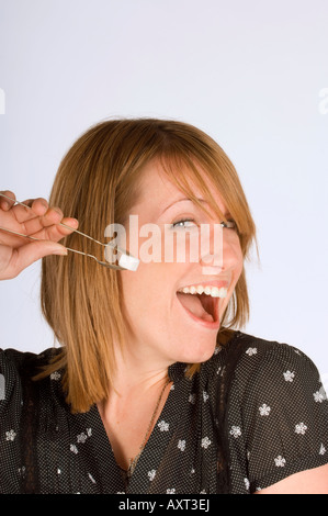 Une jeune femme heureuse avec des pinces à sucre et un cube de sucre. Banque D'Images