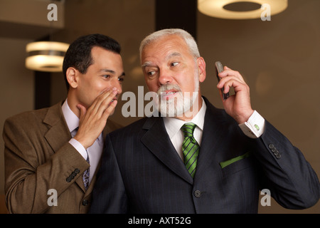 Businessman chuchotant à l'oreille de businesswoman holding a mobile phone Banque D'Images