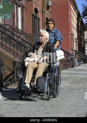 Femme bousculer une autre femme en fauteuil roulant sur un trottoir, USA, Manhattan, Harlem, New York Banque D'Images