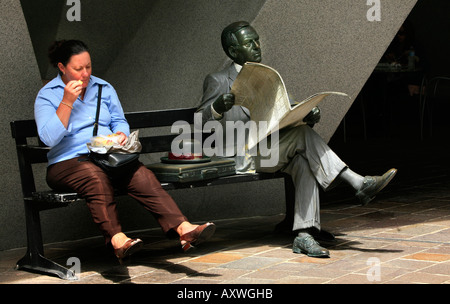Une femme assise à côté de manger son déjeuner statue d'un homme lisant un journal en Australie square Sydney Australie Banque D'Images