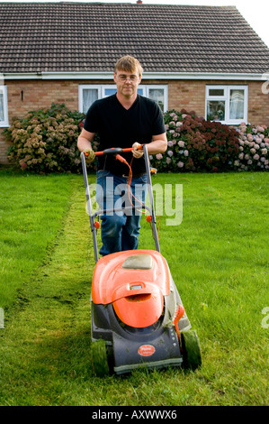 Dimanche après-midi s'aberystwyth waunfawr 1960 suburban housing estate - man mowing sa pelouse avec une tondeuse électrique orange Banque D'Images