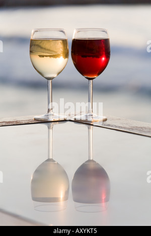 Deux glassess de vin, un rouge, un blanc sur la surface de la table de réflexion par la mer Banque D'Images