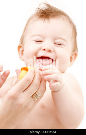 Portrait of laughing baby boy en jouant avec les mains de la mère de canard en caoutchouc Banque D'Images