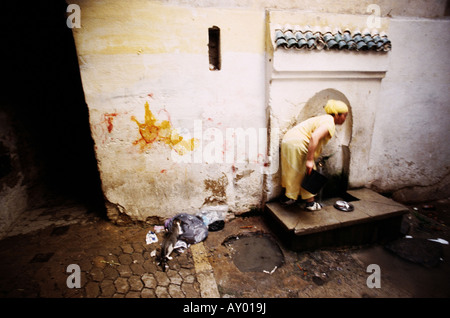 Une femme va chercher de l'eau d'un robinet public comme un chat fouille dans un sac de déchets Fez Maroc Banque D'Images