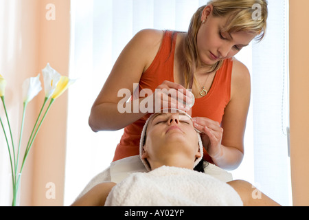 Une belle femme aux cheveux noirs reçoit un soin du visage dans une jeune blonde coiffeur Banque D'Images