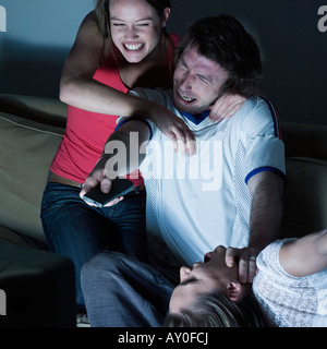 Photos dans une salle de séjour de deux jeunes filles et un homme assis sur un canapé à regarder sur tv sport event Banque D'Images