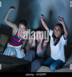 Photos dans une salle de séjour de deux jeunes filles et un homme assis sur un canapé à regarder sur tv sport event Banque D'Images