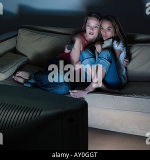 Photos dans une salle de séjour de deux jeunes filles assis sur un canapé à regarder à la télévision un film d'horreur Banque D'Images